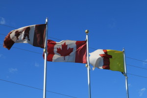 Three flags fly outside of the Hamlet office in Kugluktuk. From the left, the Kugluktuk flag, the Canadian flag, and the Nunavut flag. (Photo credit: John Kelly)